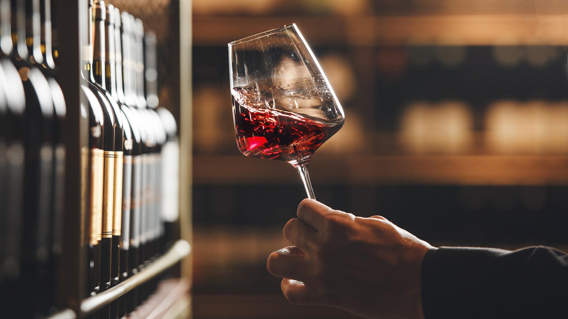 Calice di vino rosso in una cantina, mano che lo tiene delicatamente.