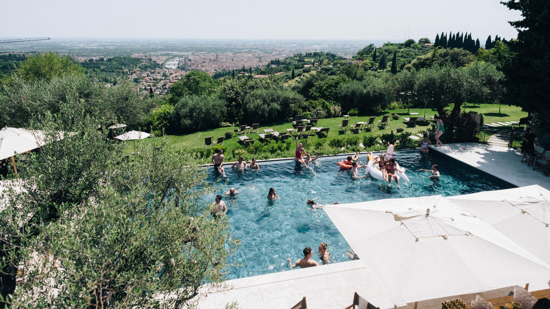 Piscina affollata con vista panoramica su una città circondata da colline verdi.