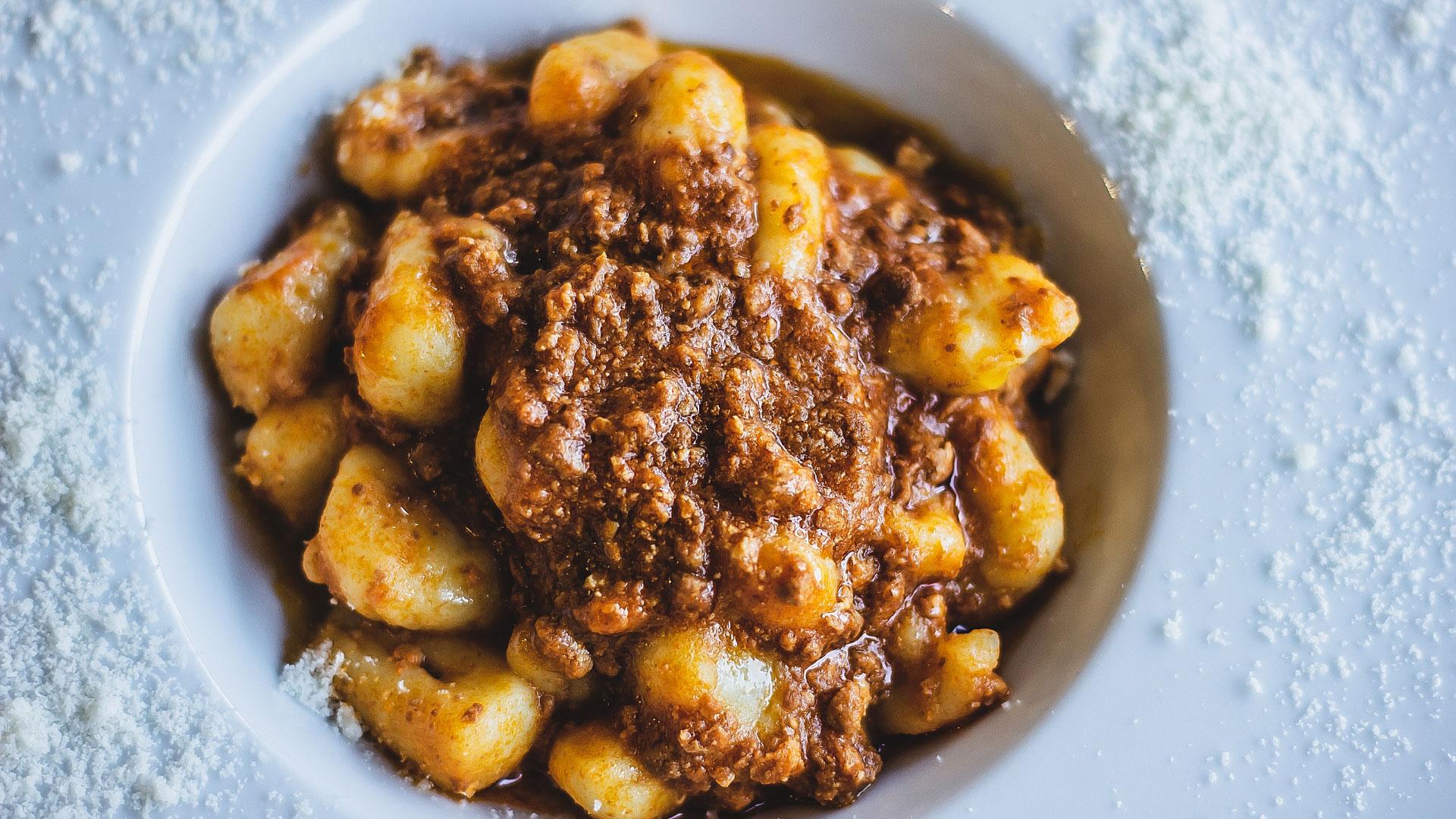 Gnocchi al ragù serviti su un piatto con formaggio grattugiato.