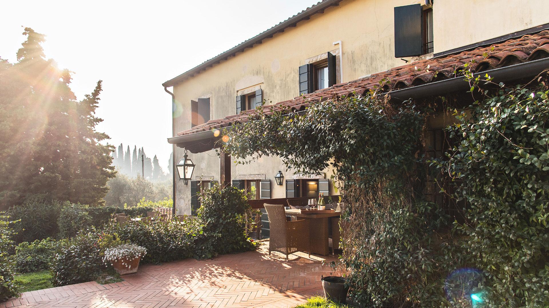 Casa rustica con giardino, terrazza coperta e piante rampicanti, illuminata dal sole.