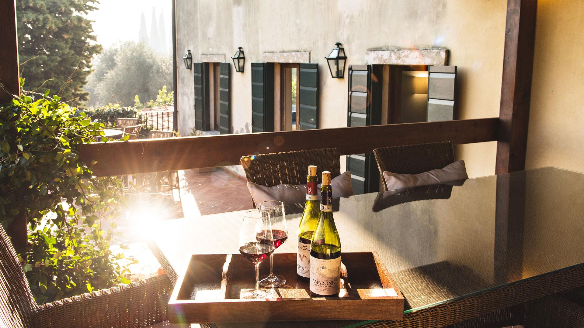 Terrazza con tavolo, vino rosso e vista su giardino al tramonto.