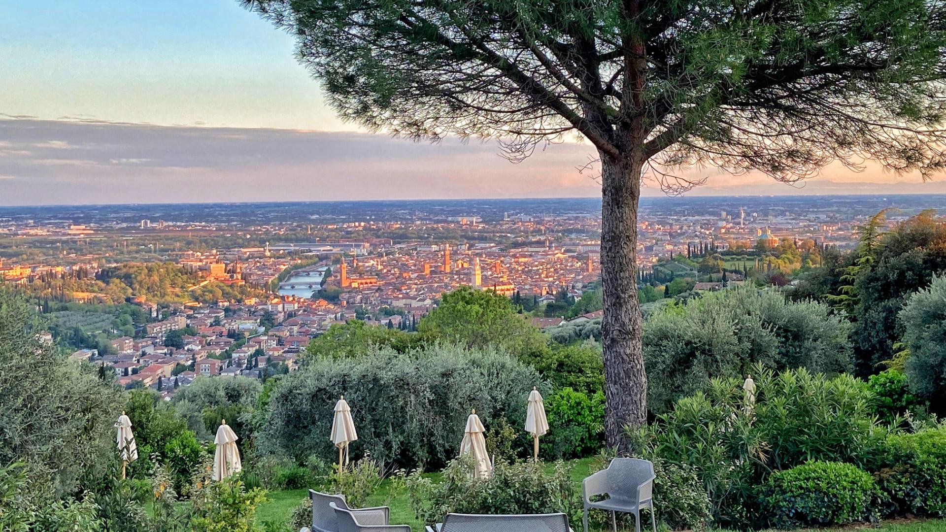 Vista panoramica su Verona al tramonto, con alberi e ombrelloni in primo piano.