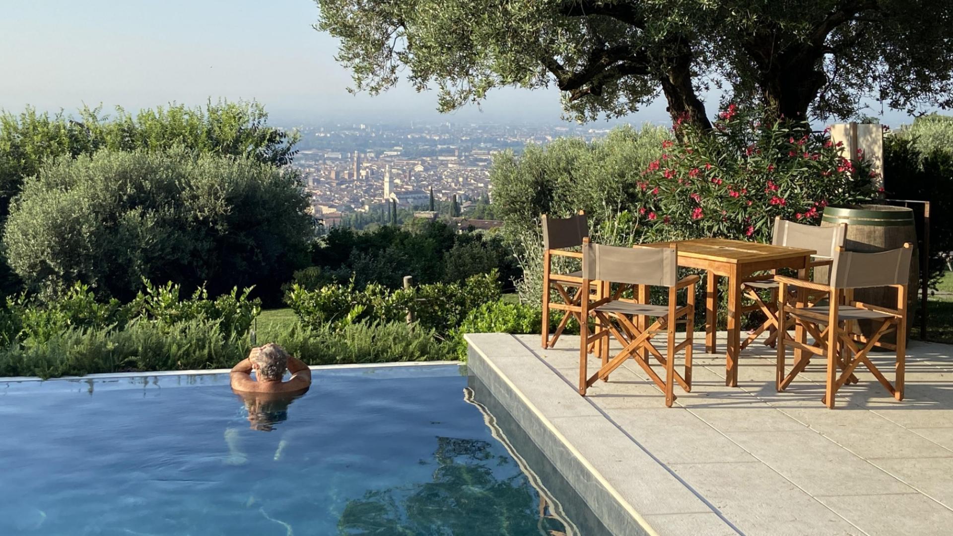 Piscina con vista panoramica sulla città, circondata da vegetazione lussureggiante e arredi da giardino.