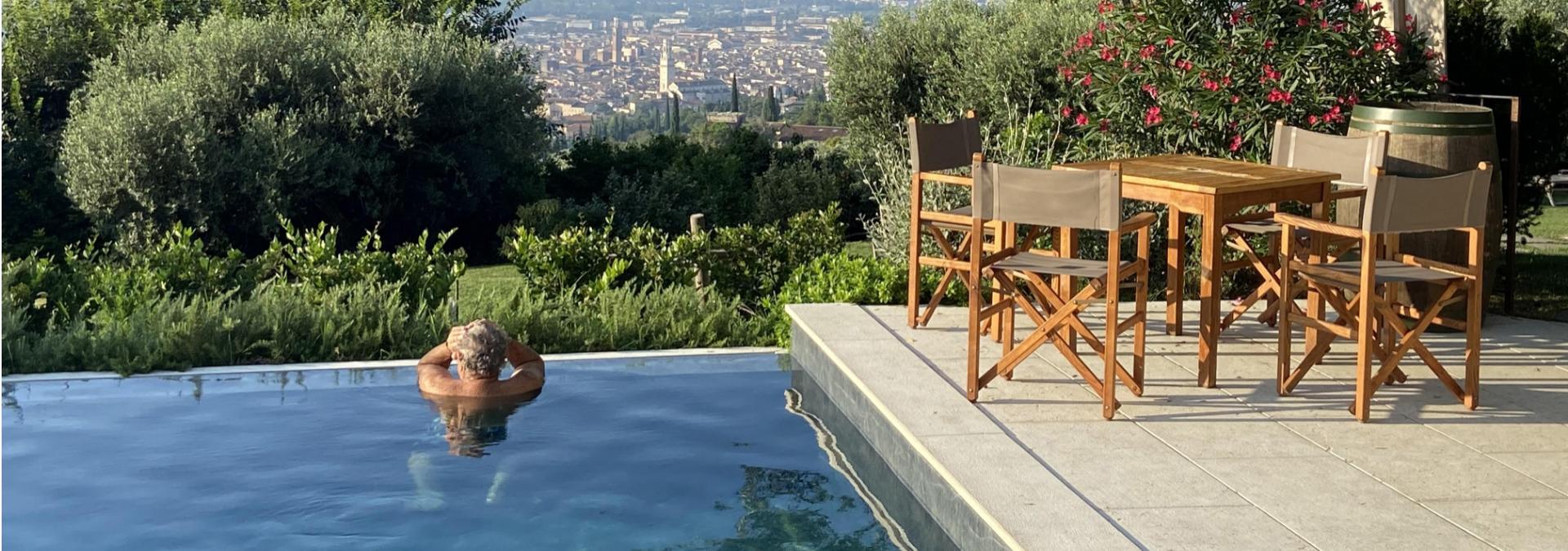 Piscina con vista panoramica sulla città, circondata da vegetazione lussureggiante e arredi da giardino.