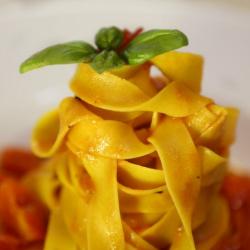 Tagliatelle al pomodoro con foglia di basilico fresco, presentate in modo elegante.