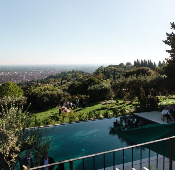 Giardino con piscina e vista panoramica sulla città, persone rilassate sui prati.