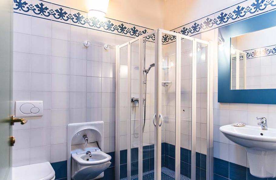 Bagno moderno con doccia, lavabo, bidet e piastrelle bianche e blu.