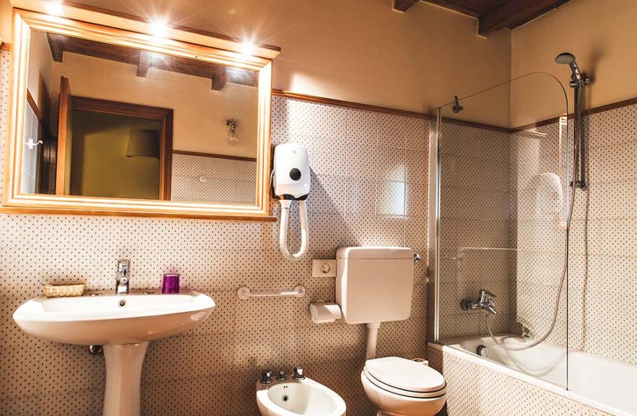 Bagno ben illuminato con vasca, lavabo, bidet, specchio grande e dispenser di sapone.