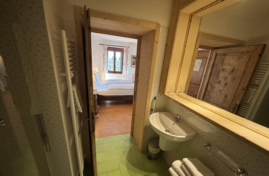 Bagno con lavabo, specchio, asciugamani e vista su camera da letto luminosa.