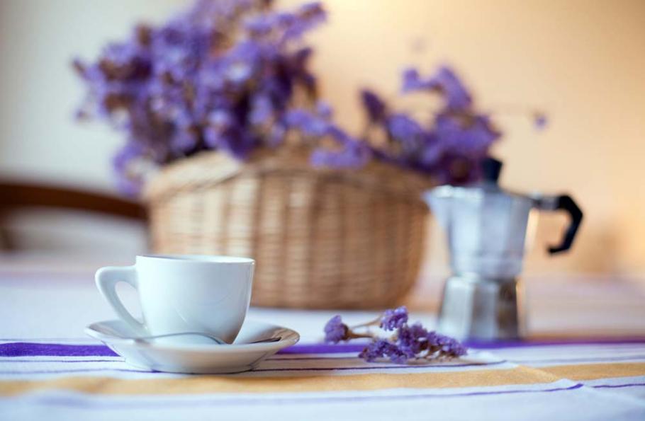 Tazza bianca su tavolo con fiori viola e moka, atmosfera accogliente.