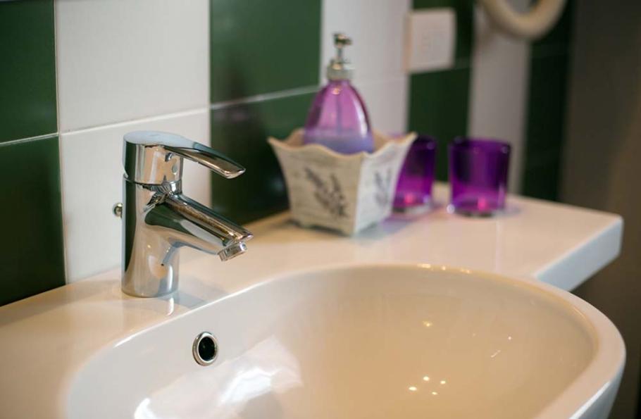 Lavabo con rubinetto cromato e accessori colorati su piastrelle verdi e bianche.