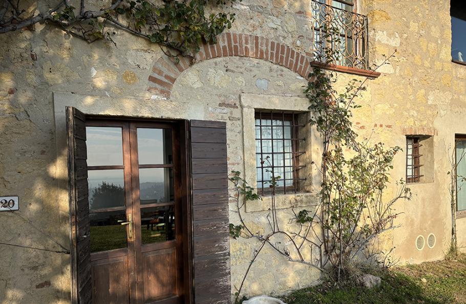 Ingresso rustico di una casa in pietra con piante rampicanti e finestre con inferriata.