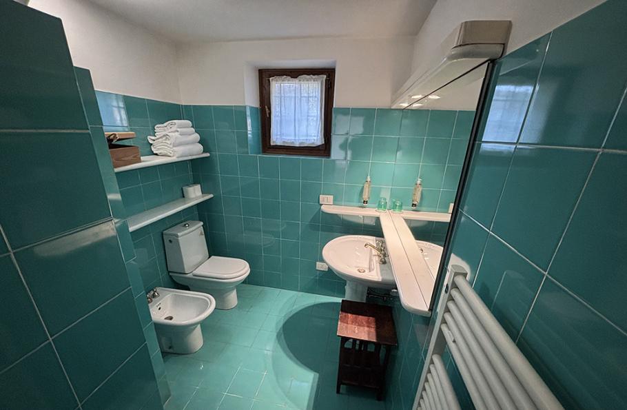 Bagno con piastrelle verdi, lavabo, bidet, WC, asciugamani e finestra.