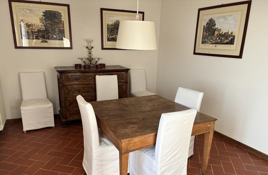 Sala da pranzo con tavolo in legno, sedie bianche e quadri alle pareti.