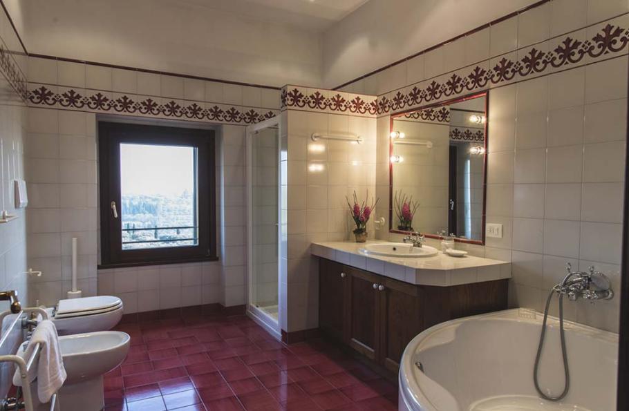 Bagno elegante con piastrelle bianche, vasca angolare, doccia, e grande specchio sopra il lavabo.