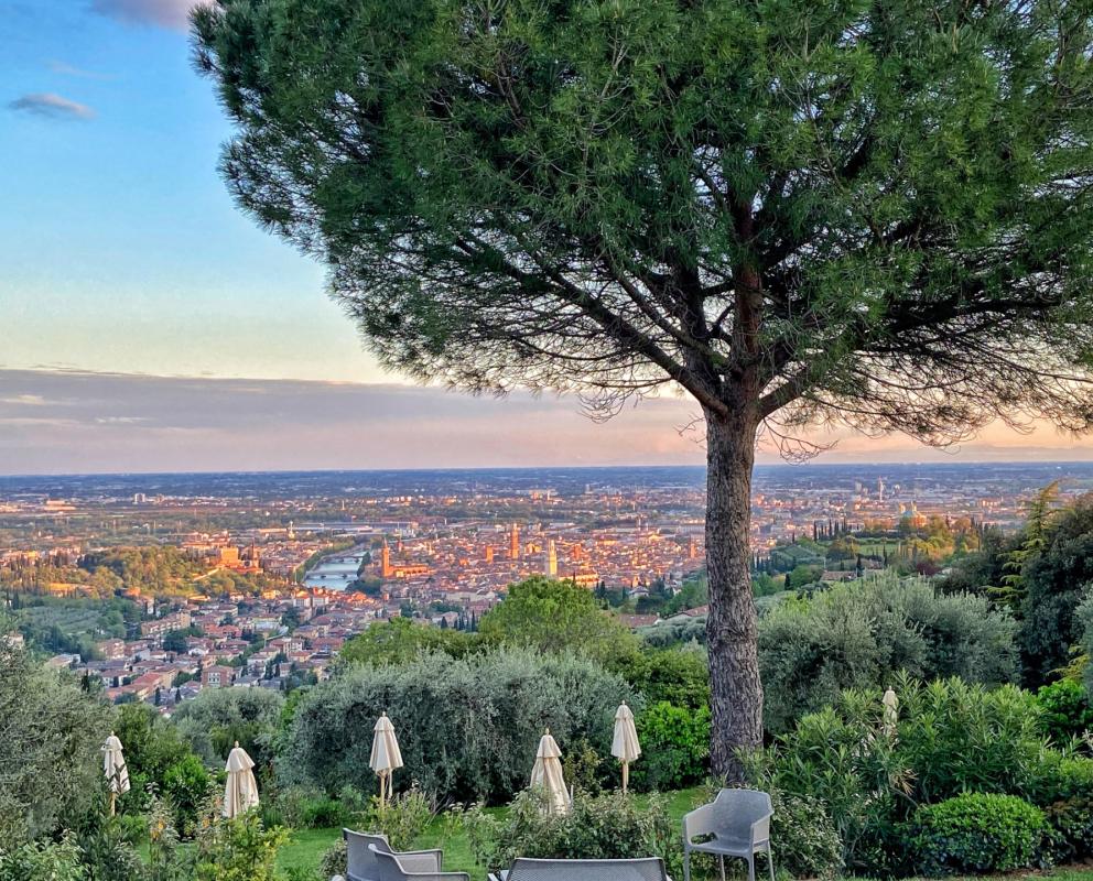 Vista panoramica su Verona al tramonto, con alberi e ombrelloni in primo piano.